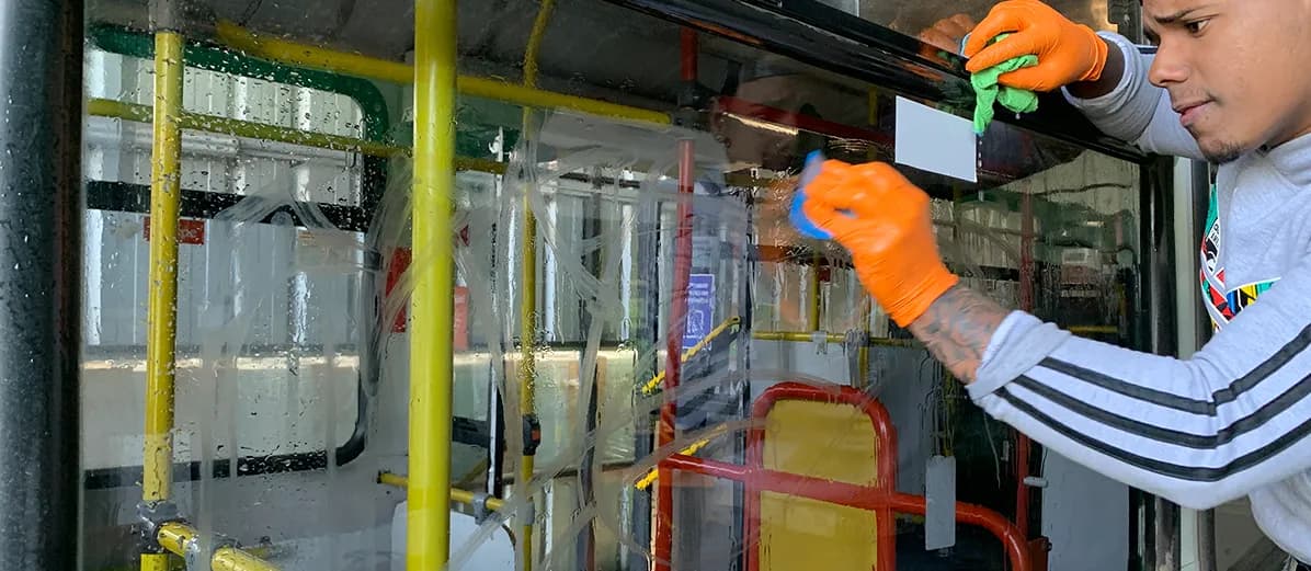 Técnico con guantes pasando un paño por un vidrio mojado con lámina transparente dentro de un bus