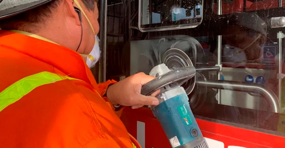 Técnico puliendo con una pulidora el vidrio de un bus para recuperarlo